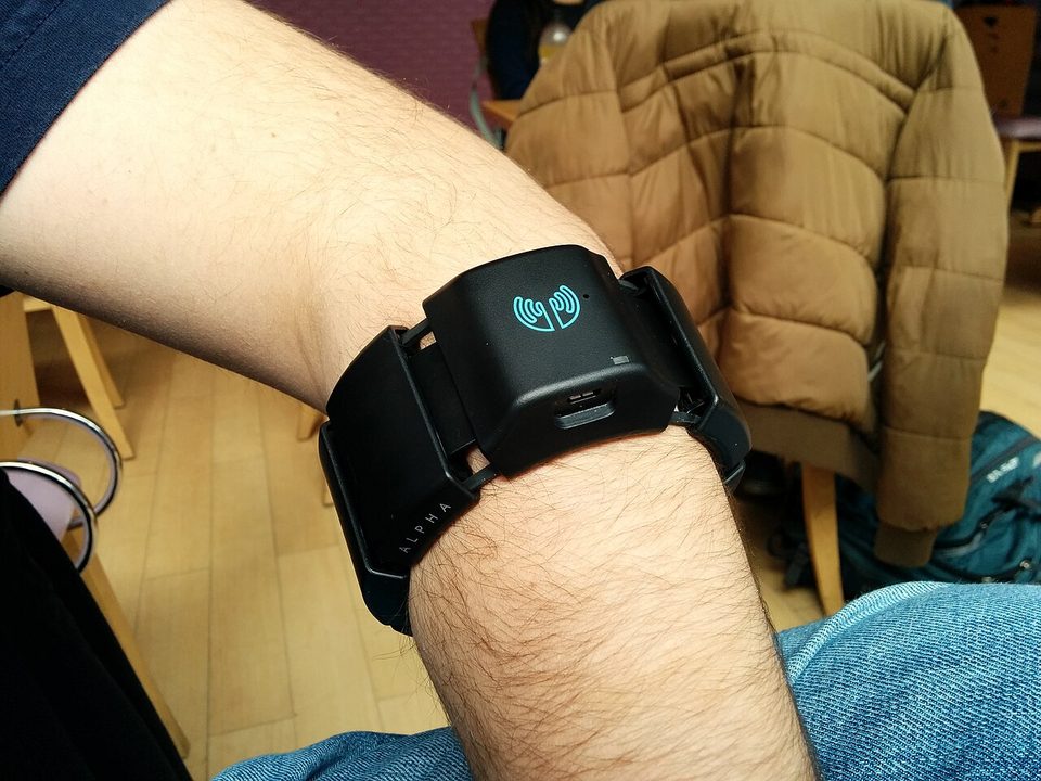 A black Myo armband worn on a bare forearm just below the elbow: eight sensor pods joined in a ring, the logo pod on top